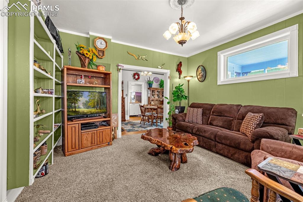 Living area with a chandelier, carpet, and ornamental molding