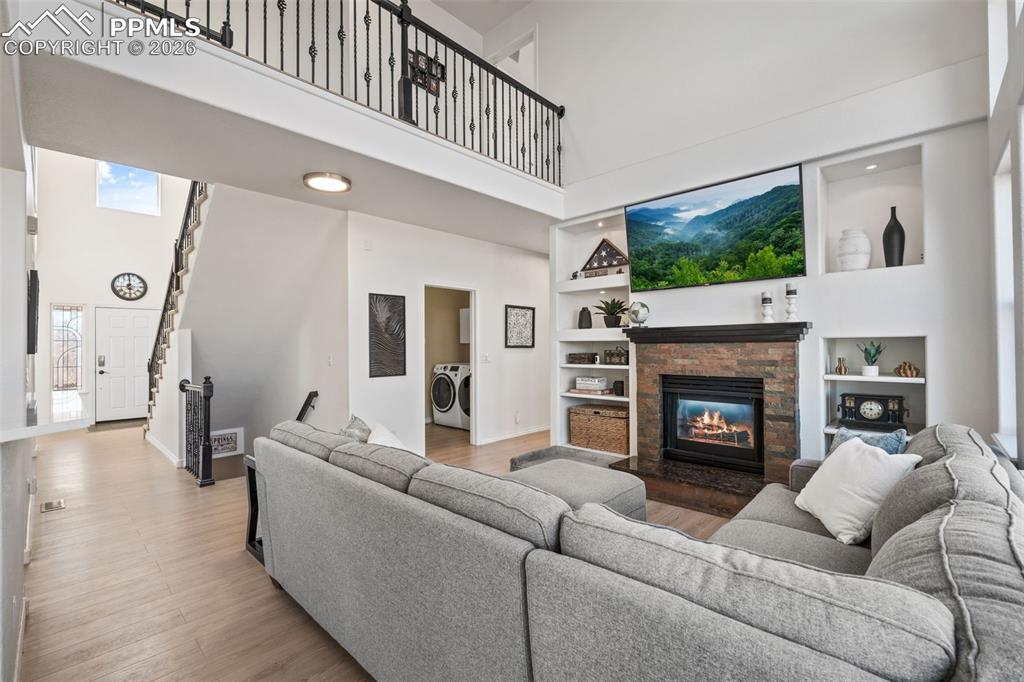 Living area featuring a high ceiling, built in shelves, a stone fireplace, and wood finished floors