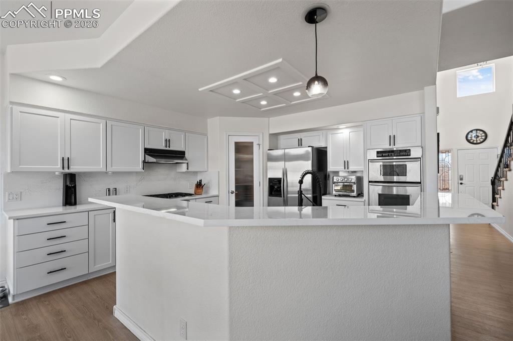 Kitchen featuring light wood-type flooring, a spacious island, stainless steel appliances, decorative light fixtures, and white cabinetry