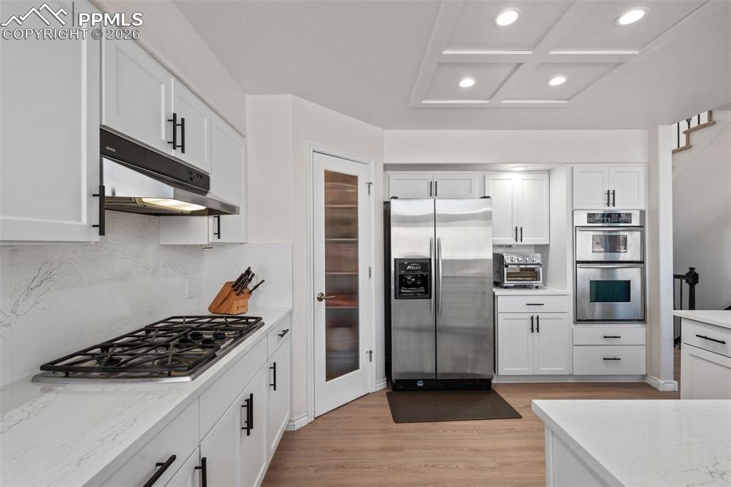 Kitchen with stainless steel appliances, white cabinetry, light wood-type flooring, light stone countertops, and recessed lighting