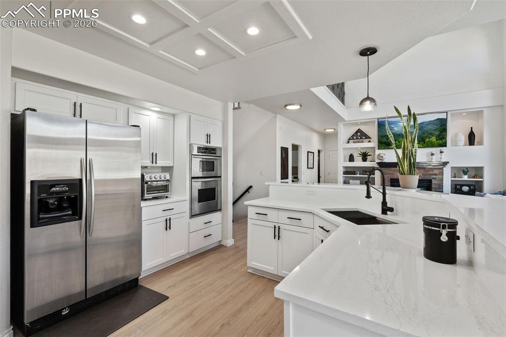 Kitchen featuring stainless steel appliances, white cabinets, open floor plan, pendant lighting, and light wood-style flooring