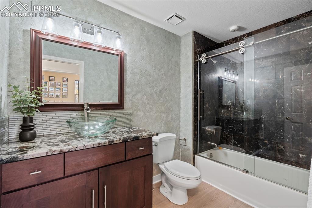 Bathroom with vanity, a textured wall, light wood finished floors, and combined bath / shower with glass door