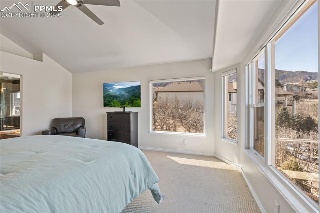 Bedroom with light colored carpet, vaulted ceiling, ceiling fan, and ensuite bathroom