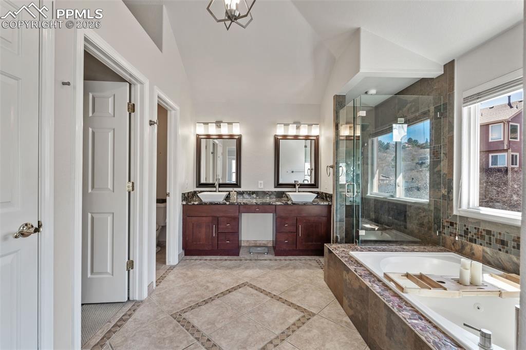 Bathroom featuring double vanity, a stall shower, a bath, lofted ceiling, and suspended lighting