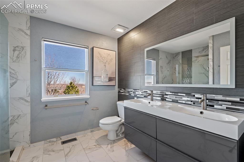 Full bath featuring double vanity, plenty of natural light, light marble finish flooring, a marble finish shower, and tile walls