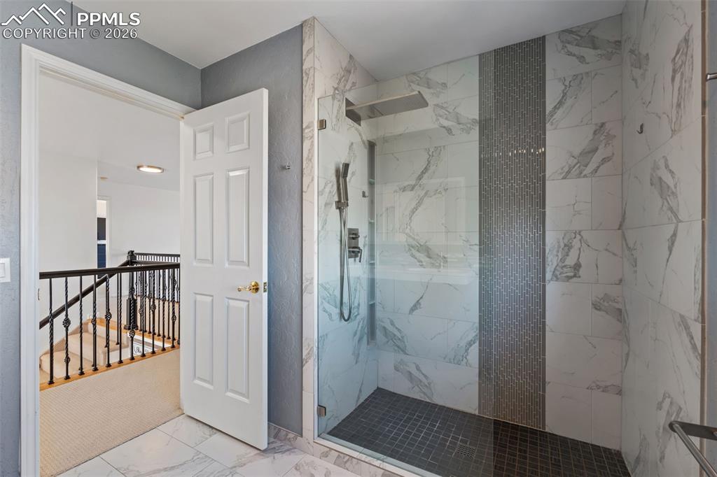 Bathroom with a marble finish shower and light marble finish flooring