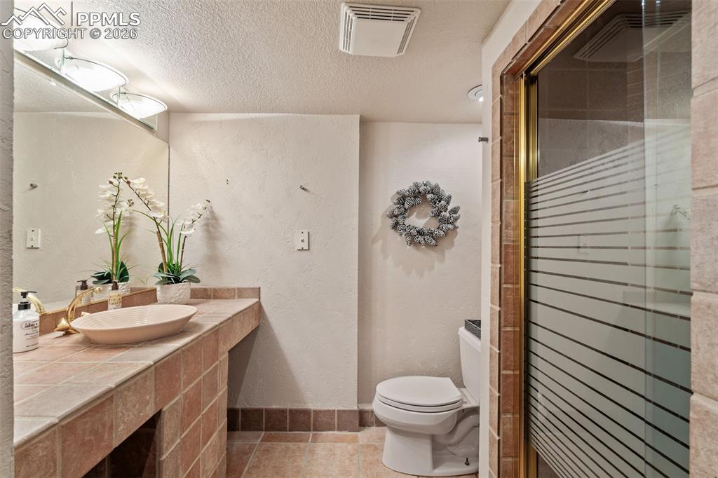 Bathroom featuring vanity, a textured wall, a textured ceiling, a stall shower, and light tile patterned floors