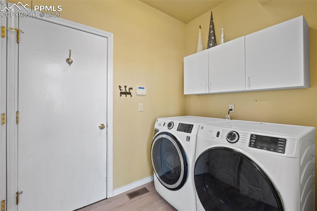 Laundry area featuring independent washer and dryer, cabinet space, and light wood-type flooring