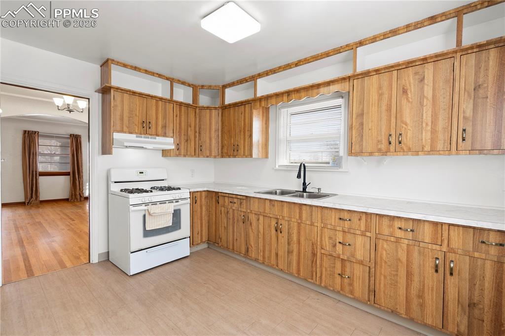 Kitchen featuring white range with gas cooktop, light countertops, light wood-type flooring, wood finish cabinetry, and arched walkways