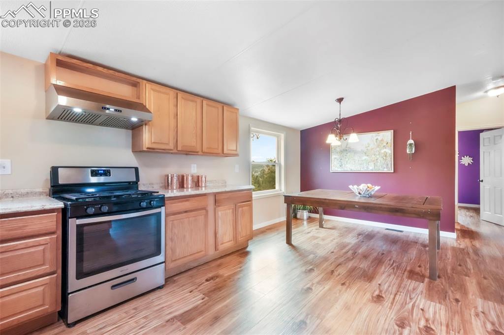 Kitchen featuring stainless steel range with gas cooktop, wall chimney exhaust hood, light wood-style flooring, light brown cabinetry, and lofted ceiling