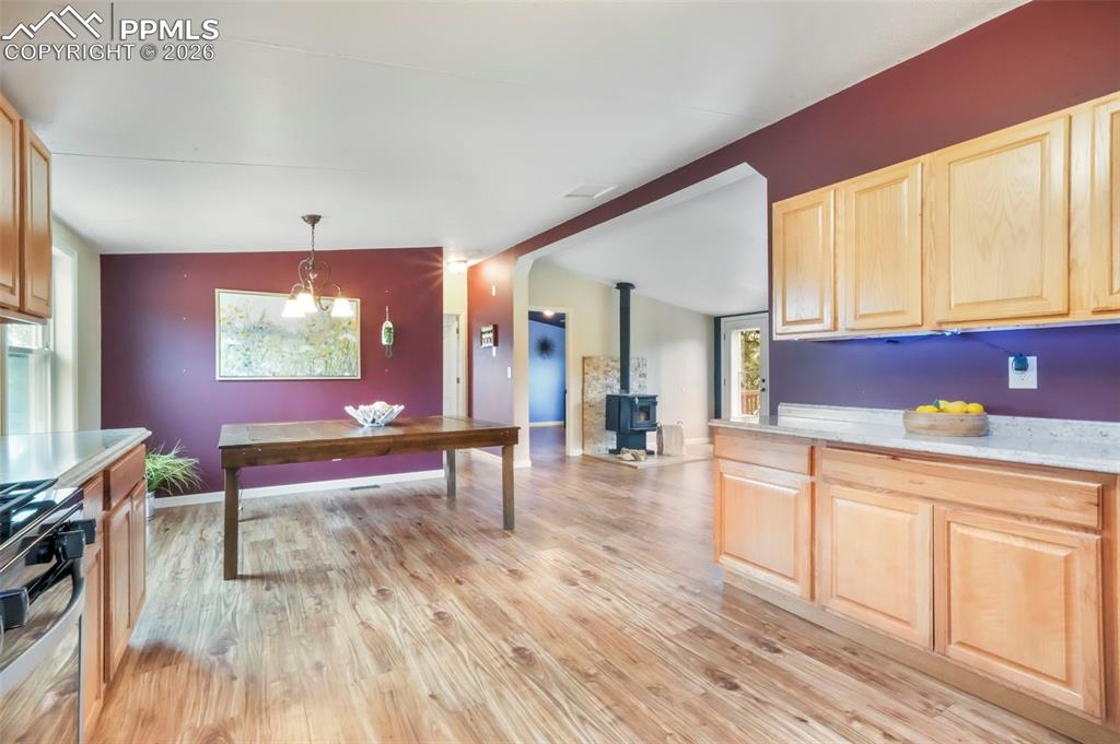 Kitchen featuring light brown cabinetry, lofted ceiling, a wood stove, stainless steel gas stove, and light wood-style flooring