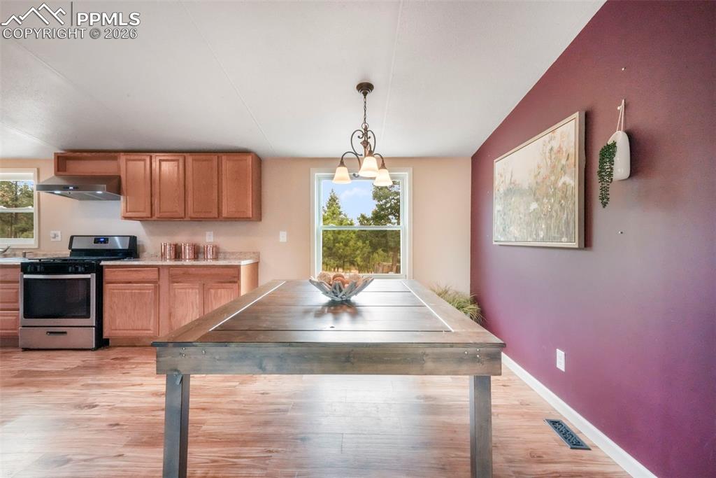 Kitchen with stainless steel gas range oven, light wood finished floors, light countertops, hanging light fixtures, and wall chimney range hood