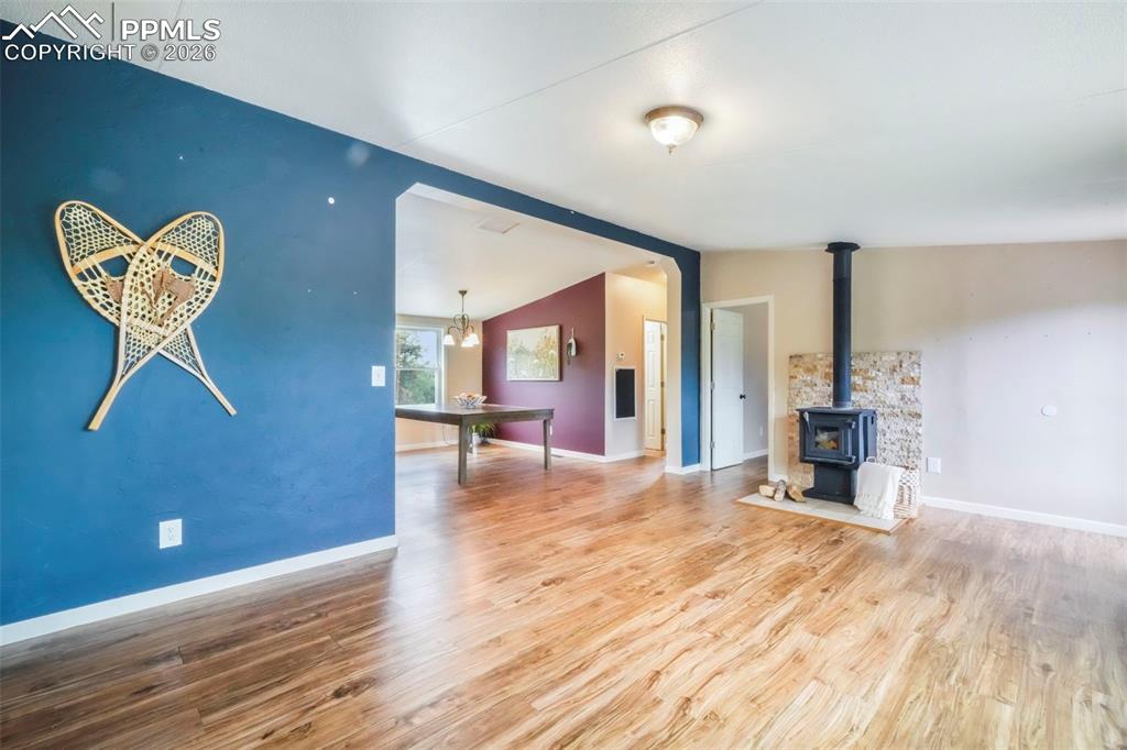 Unfurnished living room with a wood stove, wood finished floors, lofted ceiling