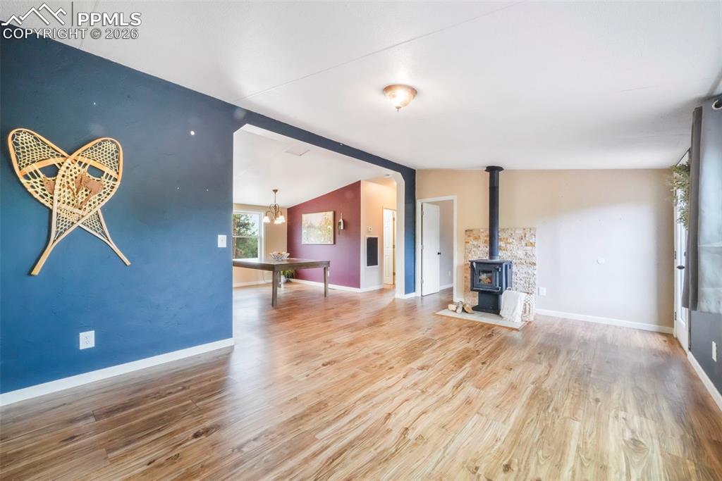 Unfurnished living room with a wood stove, light wood-type flooring, vaulted ceiling, and a chandelier