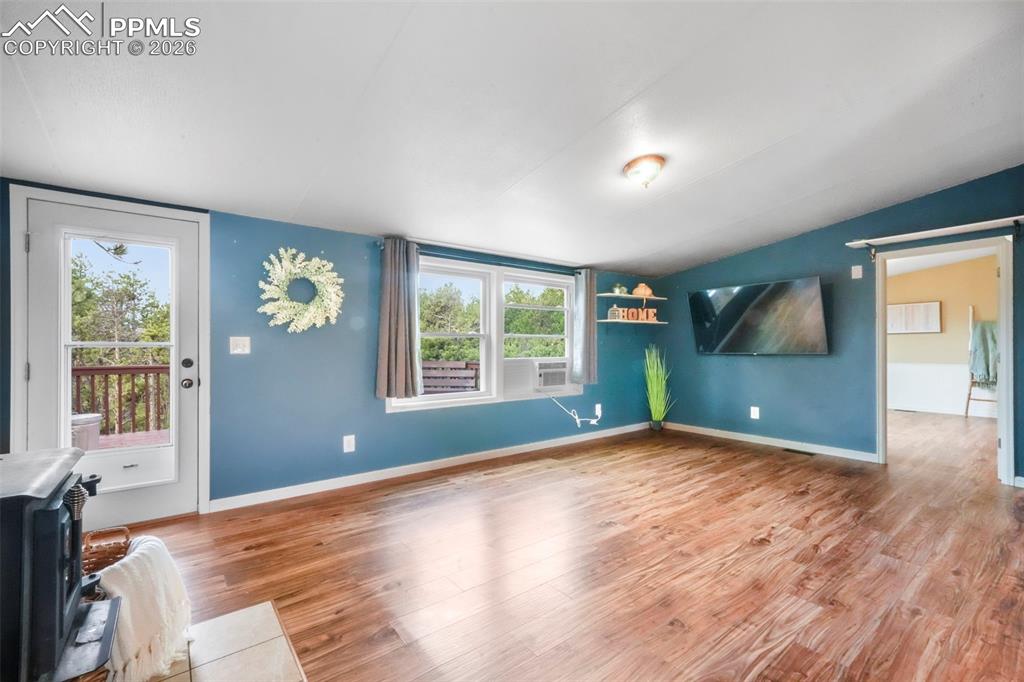 Unfurnished living room featuring wood finished floors, a wood stove, and lofted ceiling