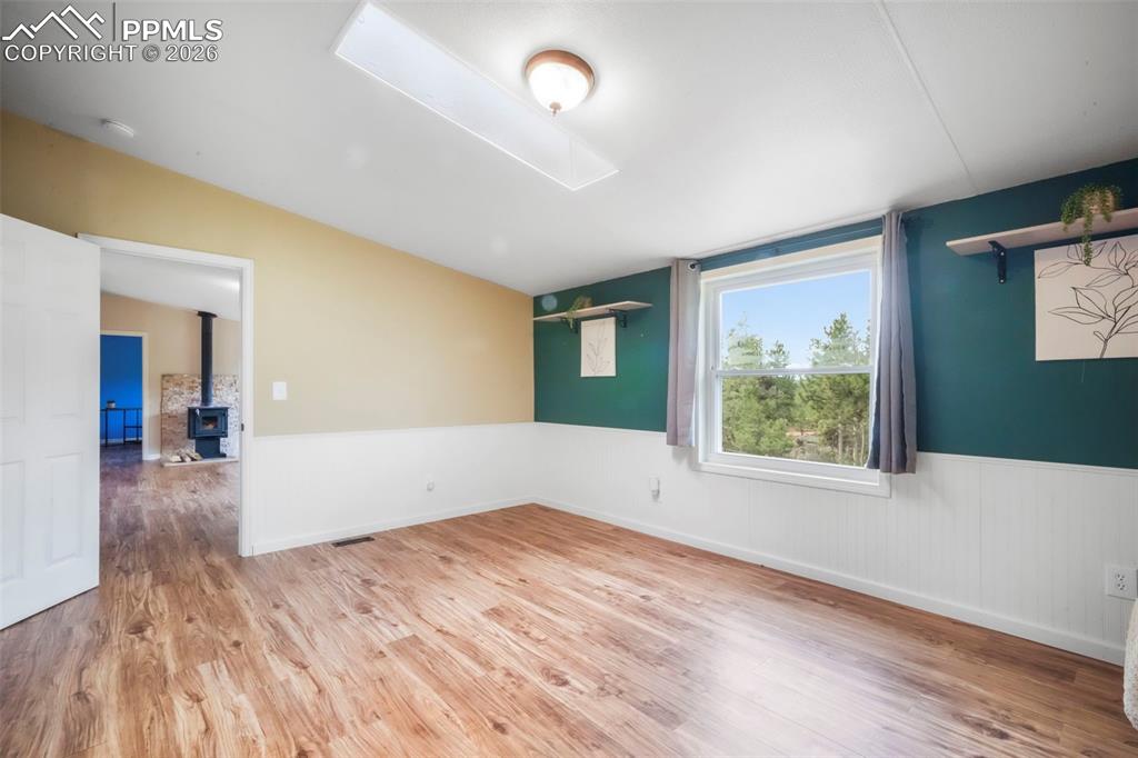 Empty room with a wood stove, light wood-type flooring, wainscoting, and a skylight