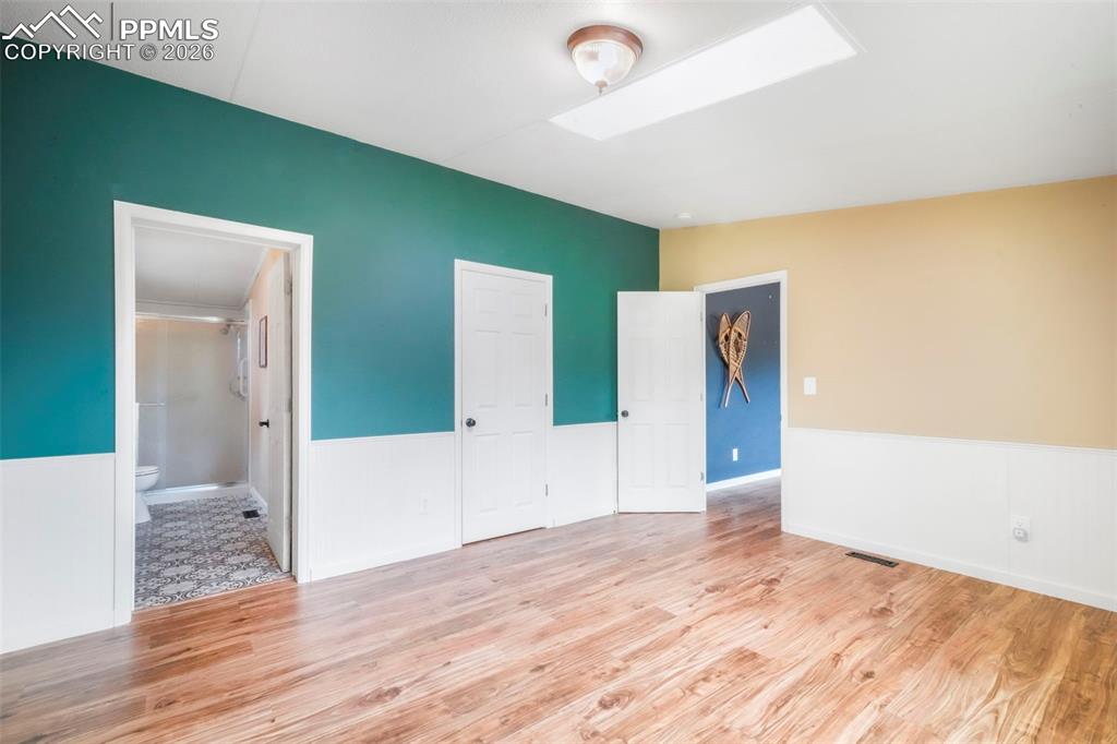 Unfurnished bedroom featuring a skylight, light wood finished floors, a wainscoted wall, and ensuite bathroom