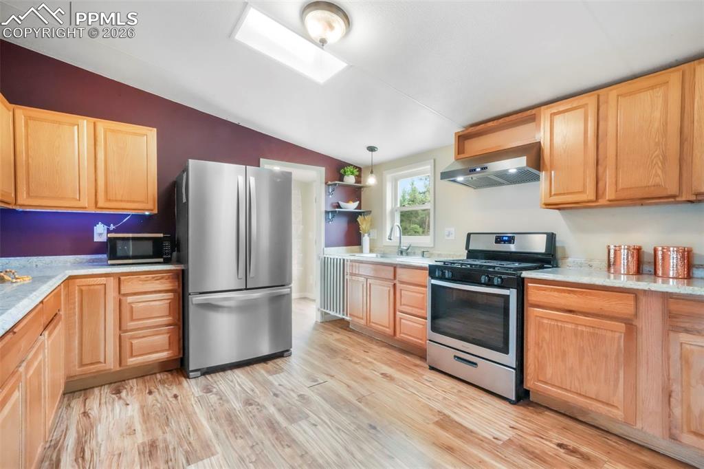 Kitchen with open shelves, stainless steel appliances, a skylight, vaulted ceiling, and light wood finished floors
