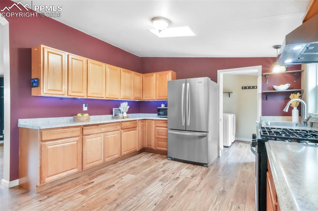Kitchen featuring stainless steel appliances, light brown cabinetry, light countertops, and exhaust hood