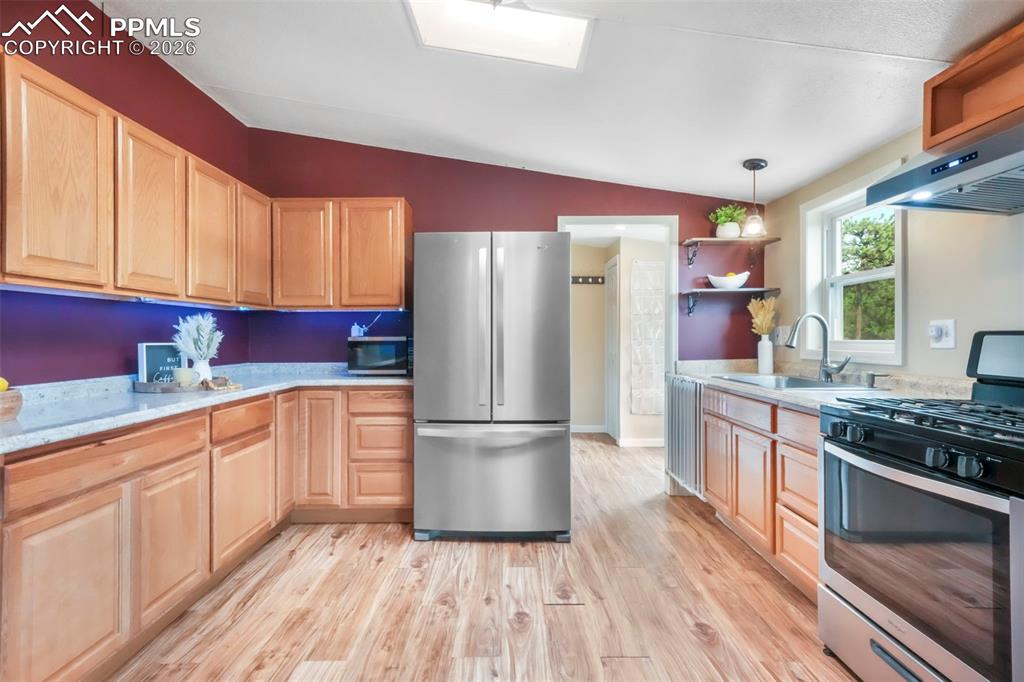 Kitchen with open shelves, stainless steel appliances, vaulted ceiling, light wood-style flooring, and pendant lighting