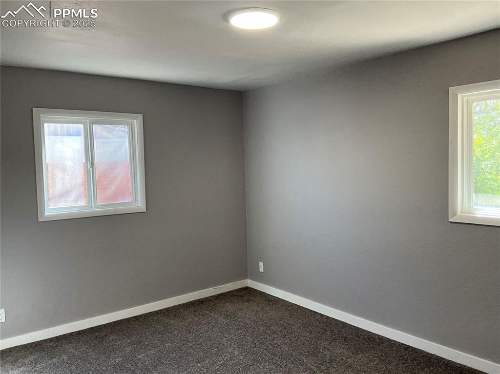 Unfurnished room with baseboards and dark colored carpet