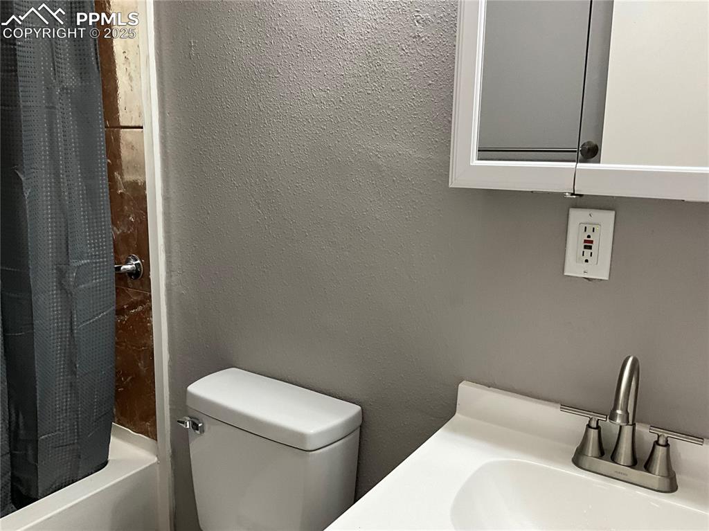 Bathroom with a textured wall, shower / bath combo with shower curtain, and vanity