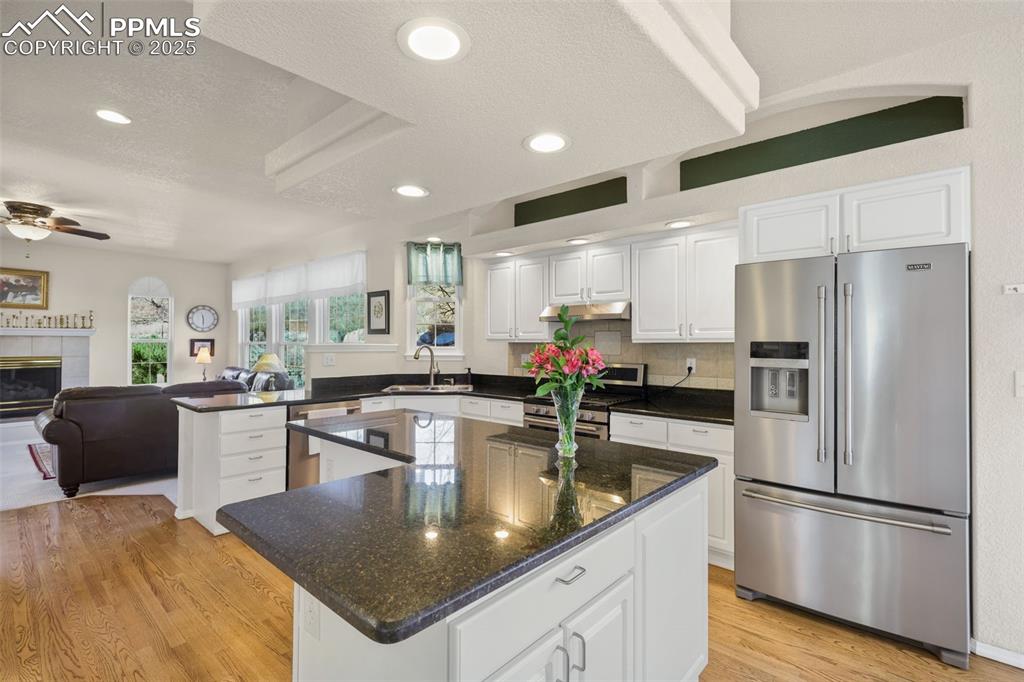 Kitchen with appliances with stainless steel finishes, white cabinets, open floor plan, a textured ceiling, and light wood-type flooring
