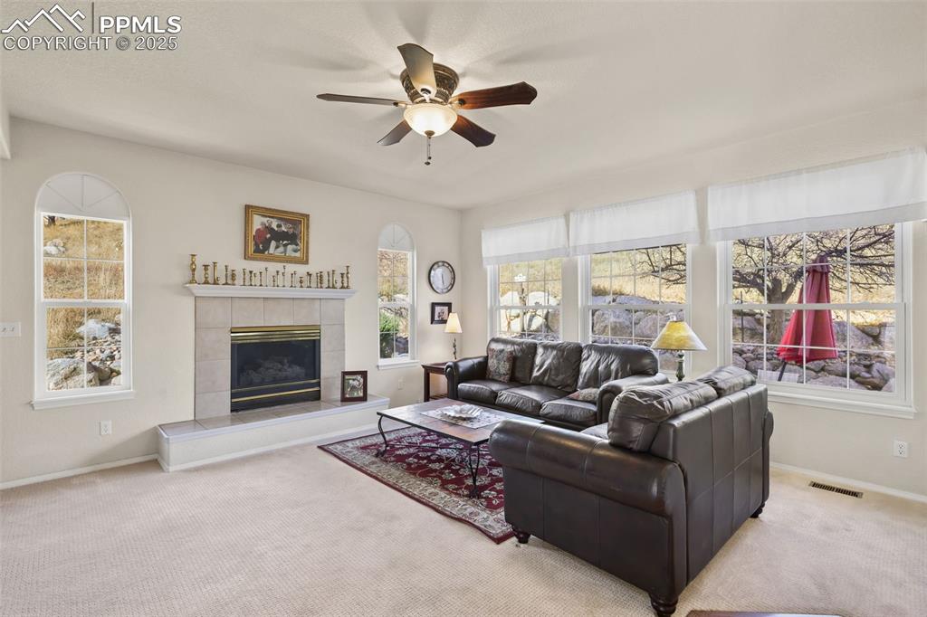 Carpeted living room featuring a tile fireplace, a ceiling fan, and plenty of natural light