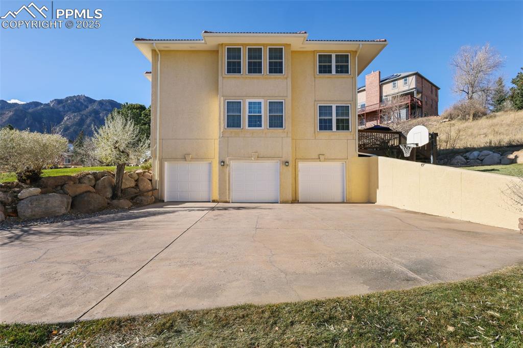 Back of house featuring concrete driveway, stucco siding, a garage, a mountain view, and a tiled roof