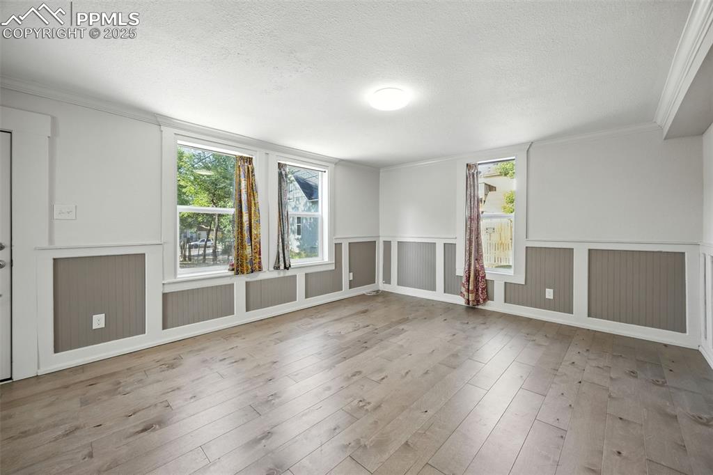 Unfurnished room with crown molding, light wood-style flooring, wainscoting, a textured ceiling, and a decorative wall