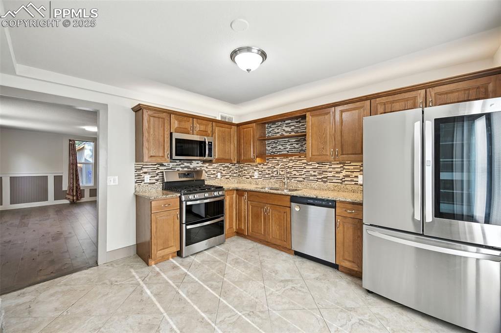 Kitchen with stainless steel appliances, light stone counters, brown cabinetry, tasteful backsplash, and light tile patterned floors