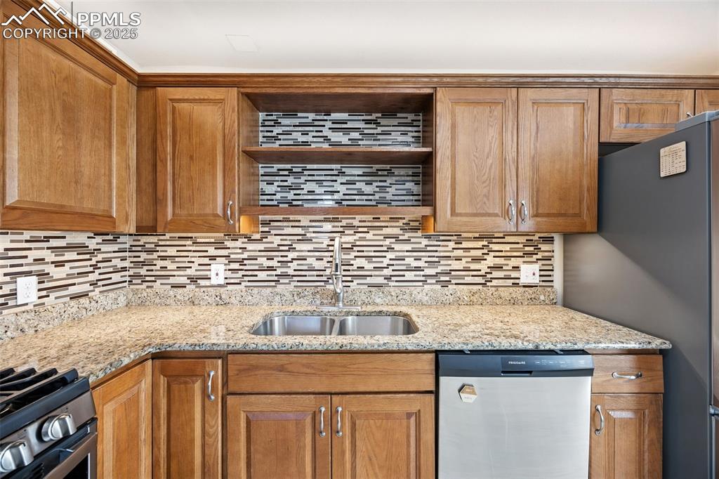 Kitchen featuring appliances with stainless steel finishes, light stone countertops, brown cabinets, and decorative backsplash