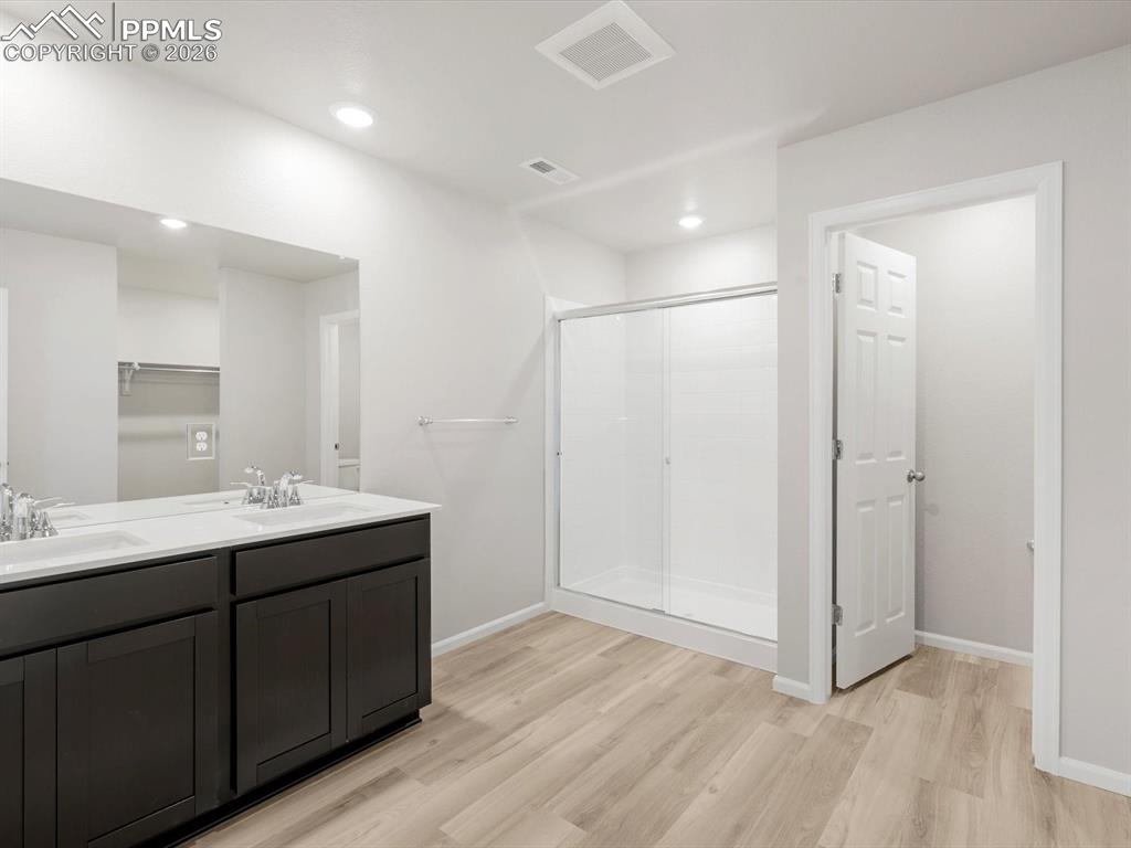 Bathroom with a stall shower, double vanity, light wood-style floors, and recessed lighting