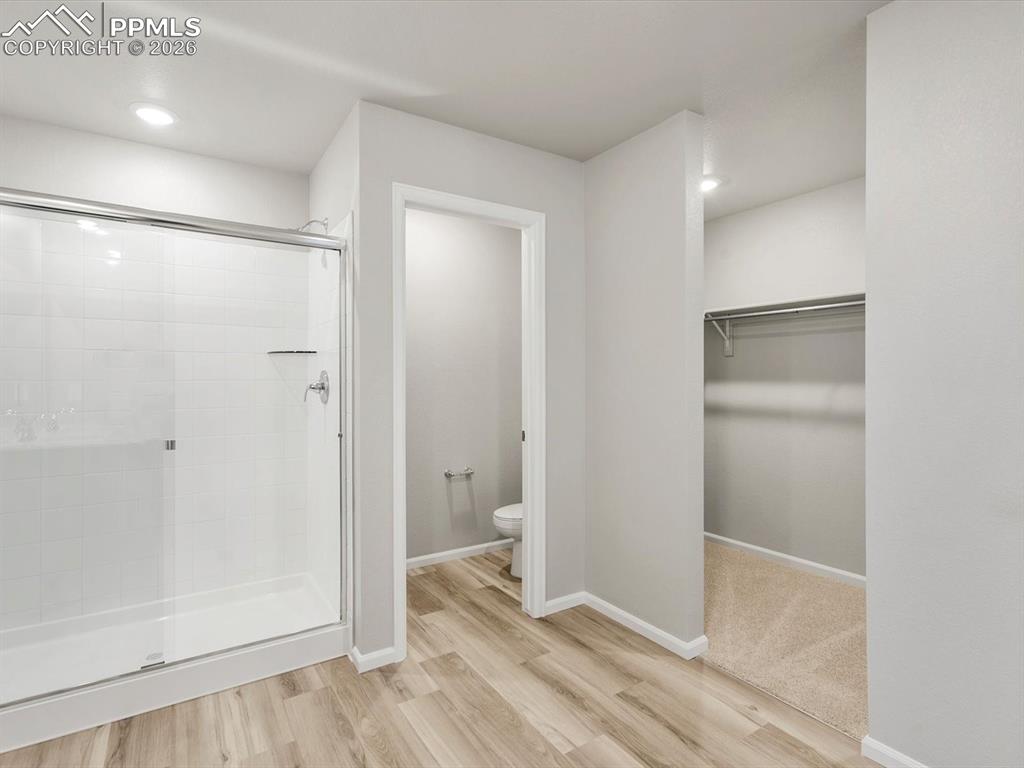 Full bathroom featuring a stall shower, a walk in closet, light wood finished floors, and recessed lighting