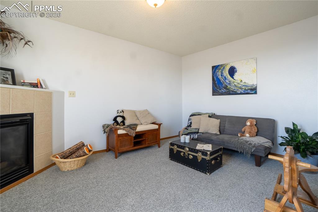 Living area with a tiled fireplace, carpet, and a textured ceiling