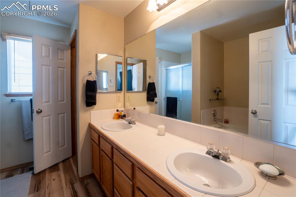 Full bathroom with double vanity, a bath, a shower stall, and wood finished floors