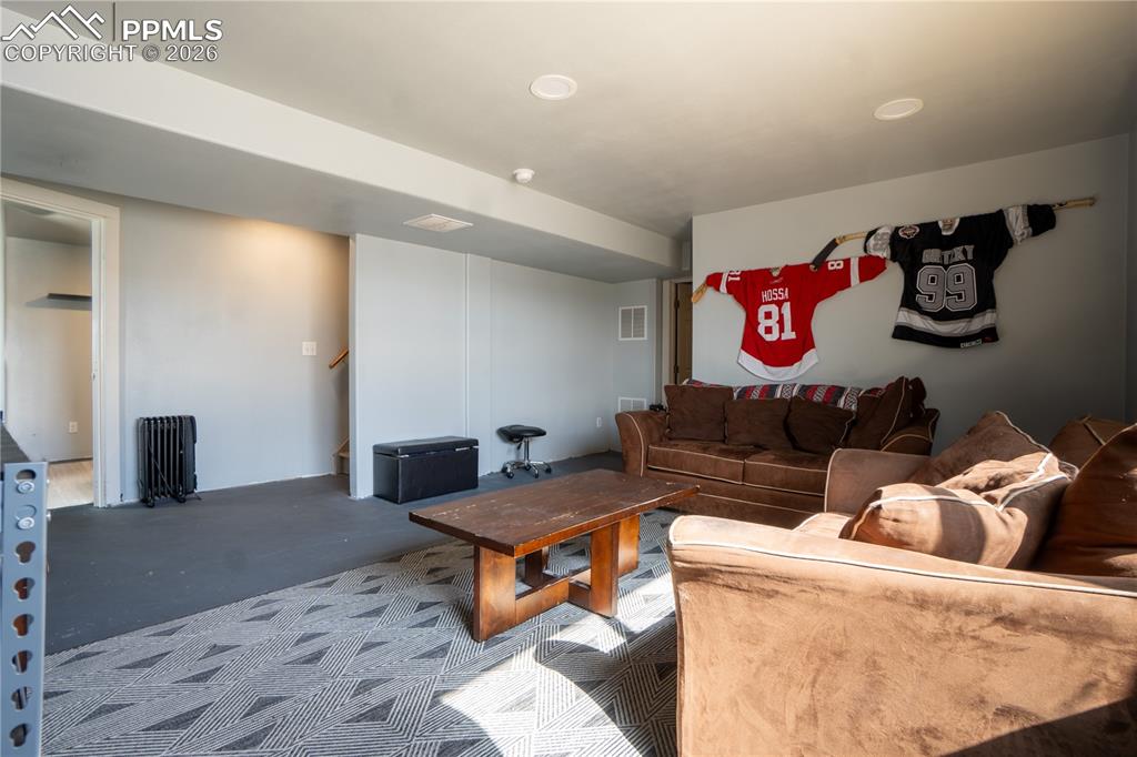 Carpeted living room featuring radiator heating unit and stairway