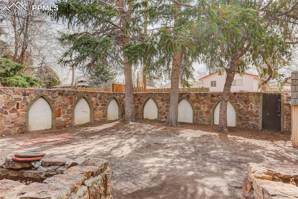 Backyard with mature trees and distinctive stone privacy wall.