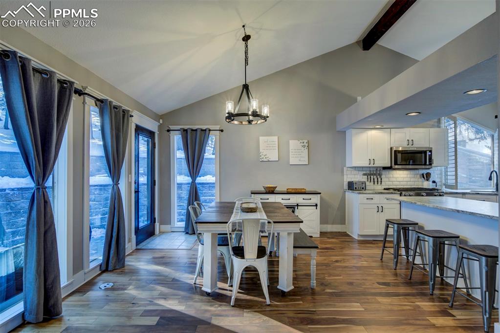 Dining space featuring a chandelier, dark wood-type flooring, plenty of natural light, beam ceiling, and high vaulted ceiling