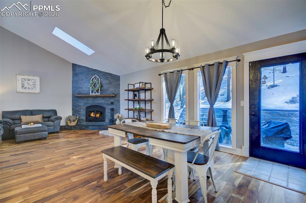 Dining room with hardwood / wood-style flooring, a fireplace, a skylight, a chandelier, and high vaulted ceiling