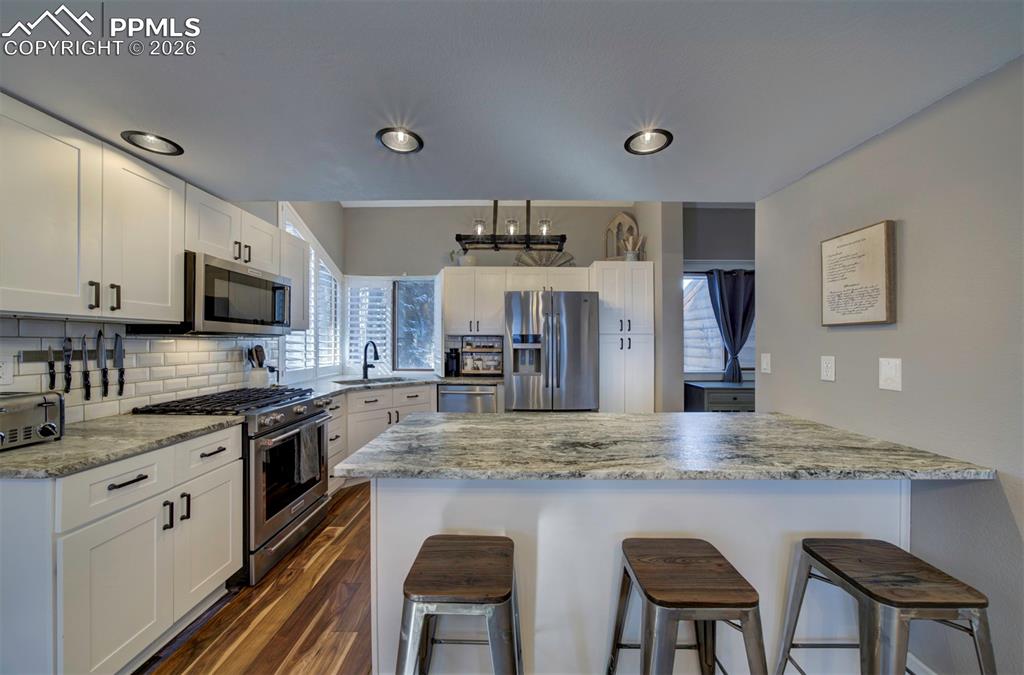 Kitchen with a peninsula, a breakfast bar, stainless steel appliances, white cabinets, and decorative backsplash