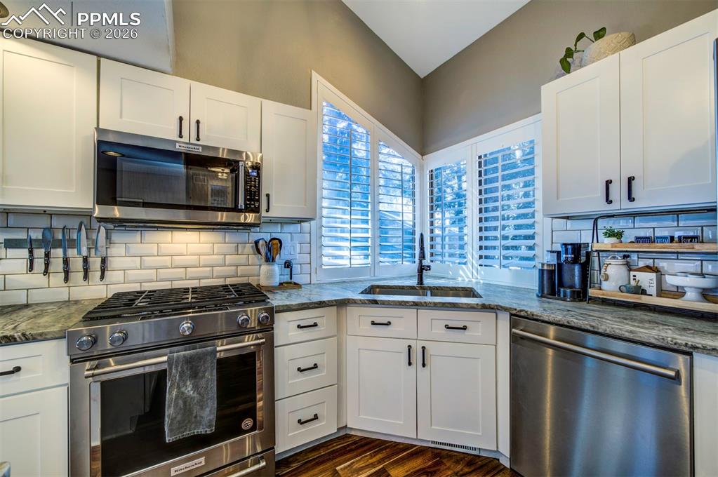 Kitchen with stainless steel appliances, white cabinetry, and dark stone counters