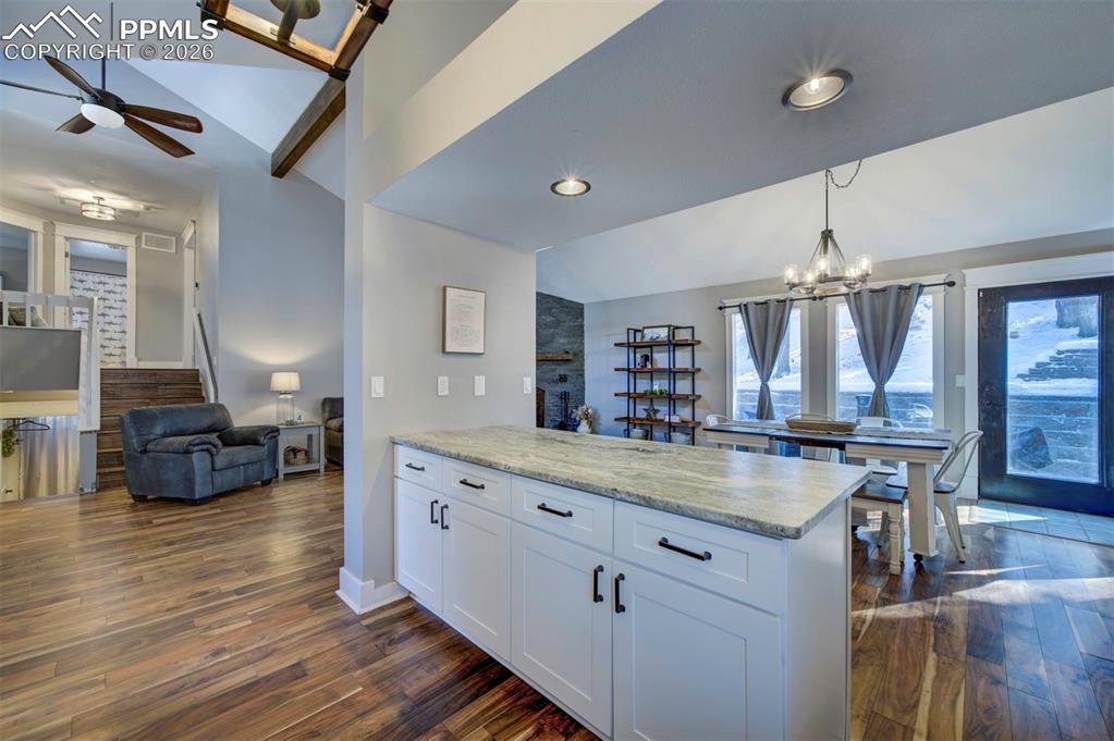 Kitchen featuring vaulted ceiling, a chandelier, white cabinets, open floor plan, and dark wood-style flooring