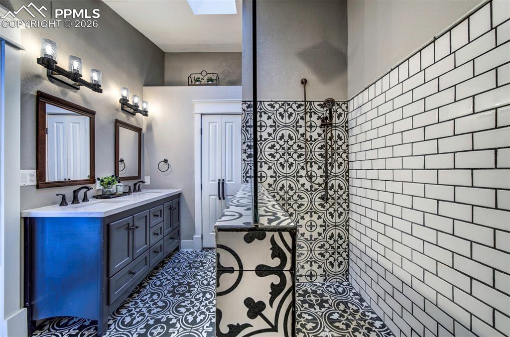 Full bath featuring double vanity, tiled shower, a skylight, and dark tile patterned floors