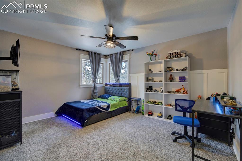Bedroom featuring carpet, a ceiling fan, and a wainscoted wall