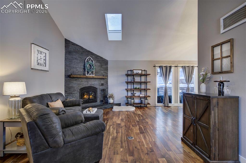 Living room with a skylight, high vaulted ceiling, dark wood-type flooring, and a fireplace