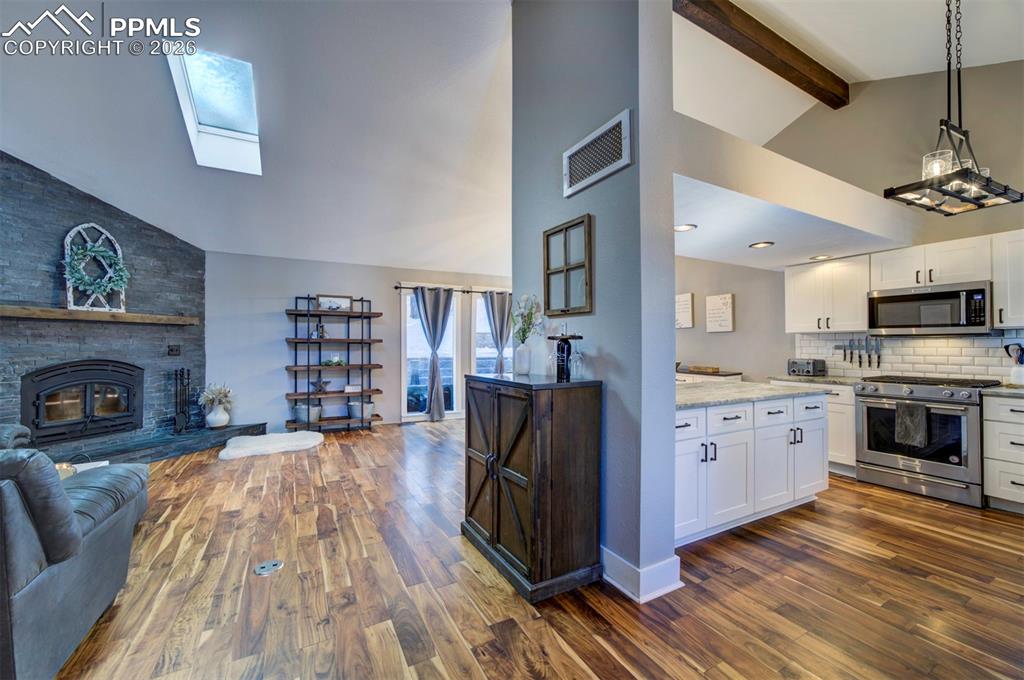 Kitchen featuring a skylight, stainless steel appliances, high vaulted ceiling, white cabinets, and beamed ceiling
