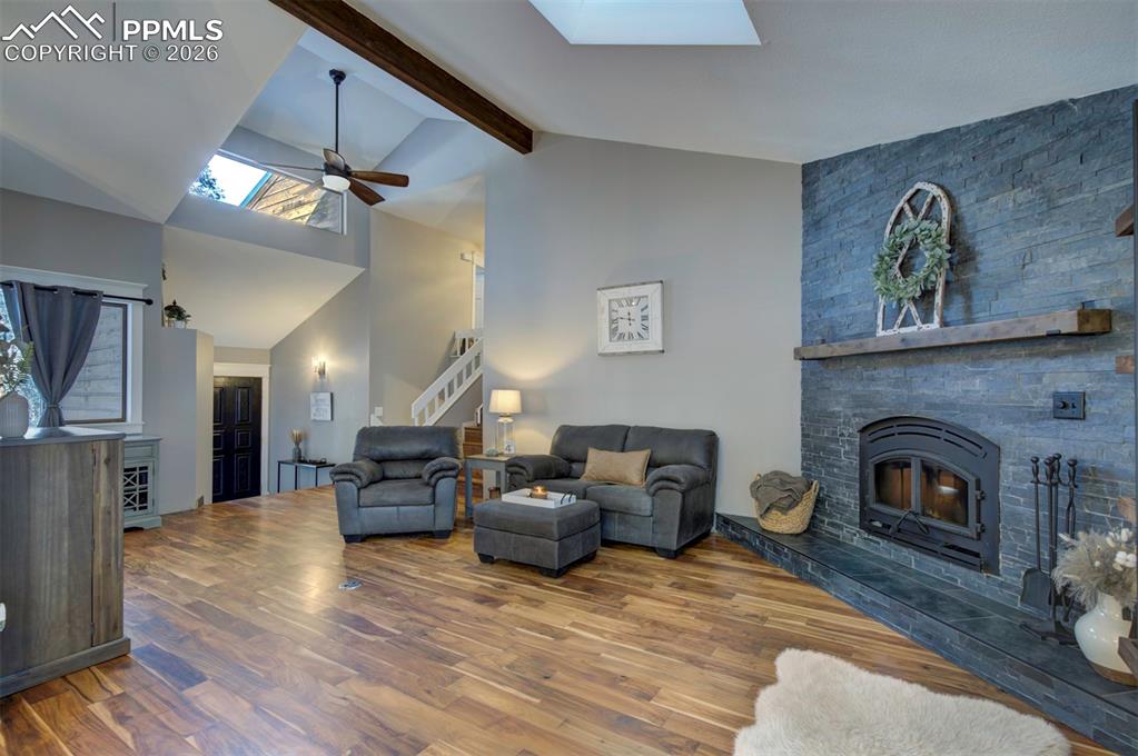 Living room featuring a skylight, beamed ceiling, a ceiling fan, high vaulted ceiling, and wood finished floors