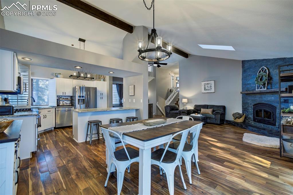 Dining space featuring a chandelier, dark wood finished floors, beamed ceiling, stairs, and a fireplace