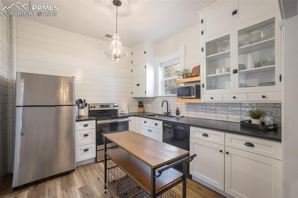 Kitchen featuring white cabinetry, stainless steel appliances, pendant lighting, and dark countertops